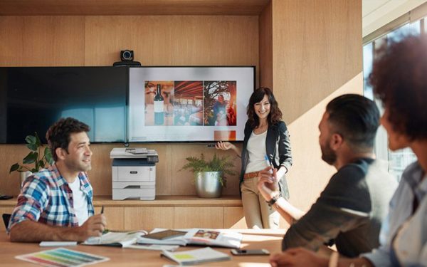 Smiling work team in front of a screen next to a Xerox® B305 multifunction printer