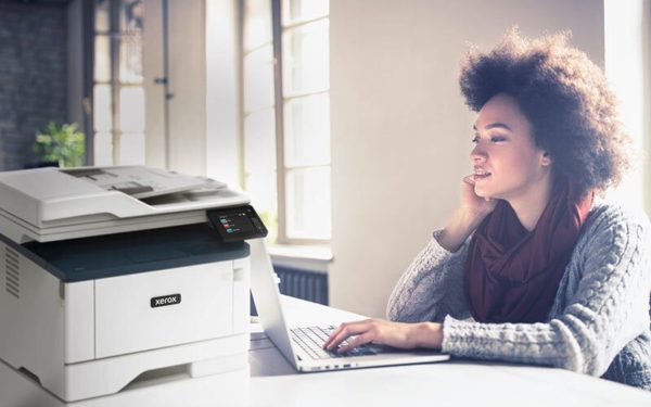 Junge Frau, die an ihrem Computer neben einem Multifunktionsdrucker Xerox® B315 arbeitet.