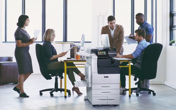 Teamarbeit in einem Büro mit bedruckten Papieren und dem Farb-Multifunktionsdrucker Xerox® VersaLink® C7100 Series